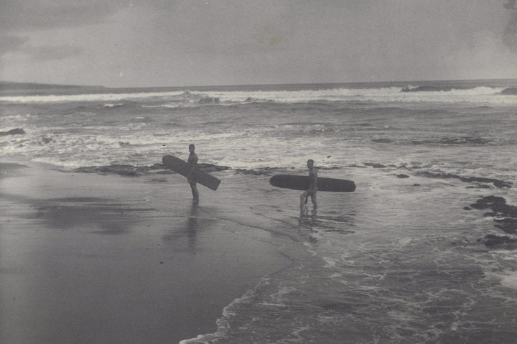 Hawaii, 1890s: two Polynesian natives carry their surfboards on a sandy beach at Hilo Bay | Photo: Herbert Smith